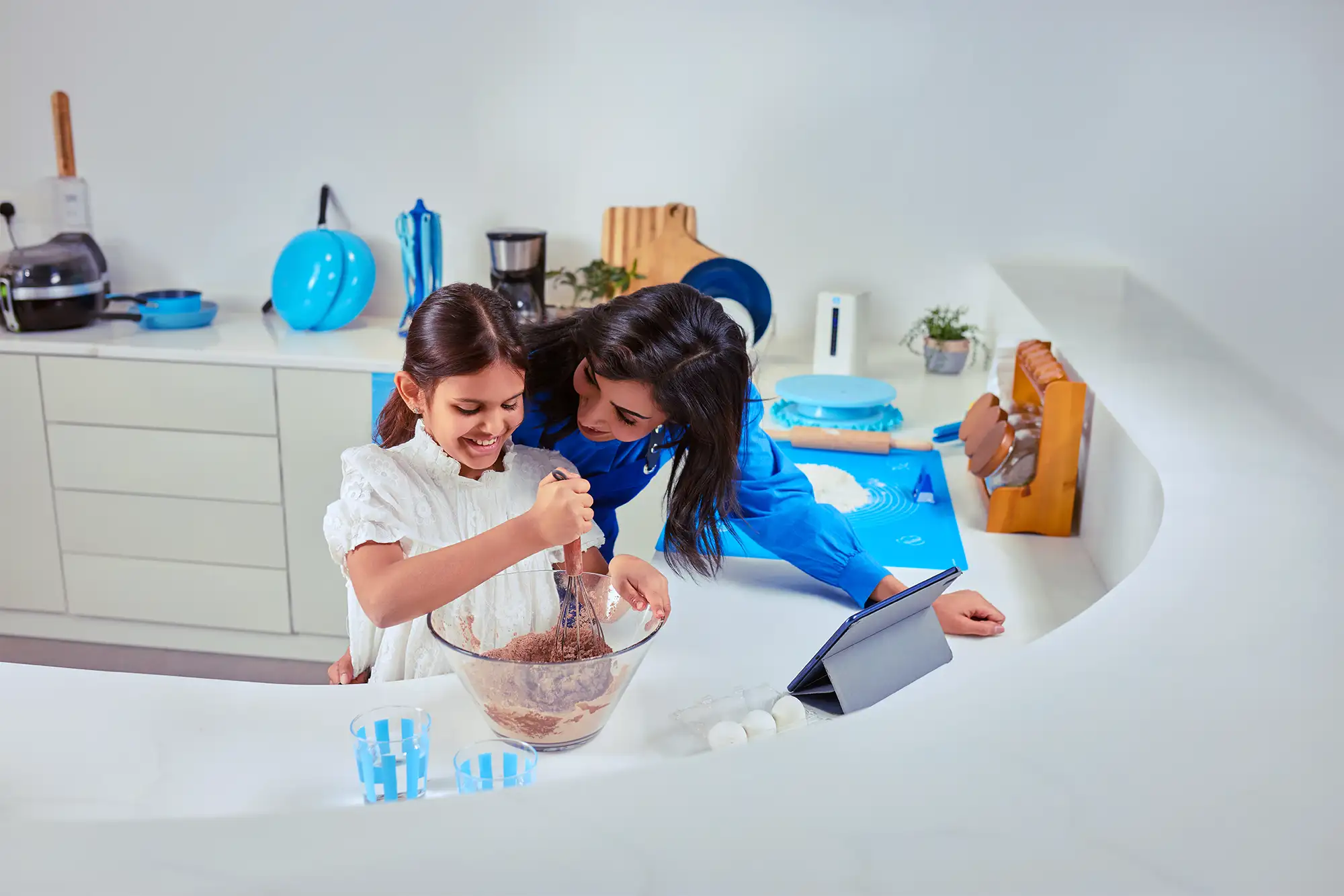 Family baking together in a bright kitchen with a tablet on the counter